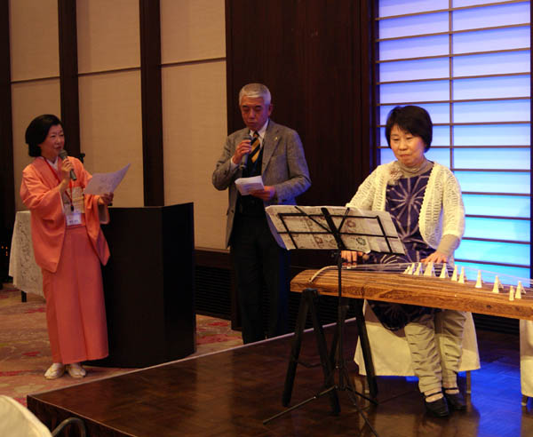 西田会員の琴演奏で合唱　リードする野津隆会員と司会の岸本幸子理事